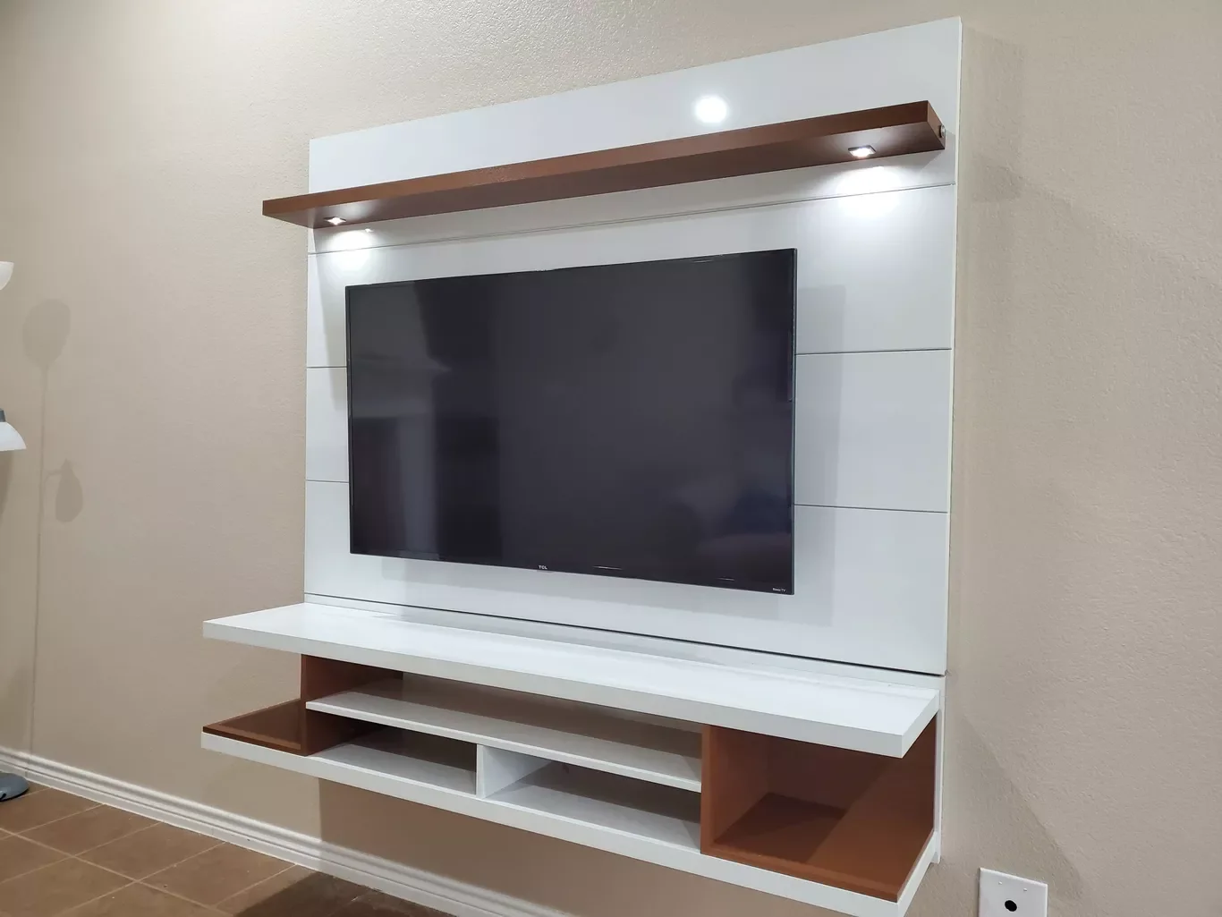 Modern wall-mounted entertainment center with a flat-screen TV and wooden shelves with built-in lighting.