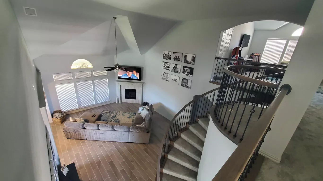 View of a living room from the staircase, featuring a sectional sofa, a fireplace, wall-mounted TV, framed photos, and a ceiling fan.