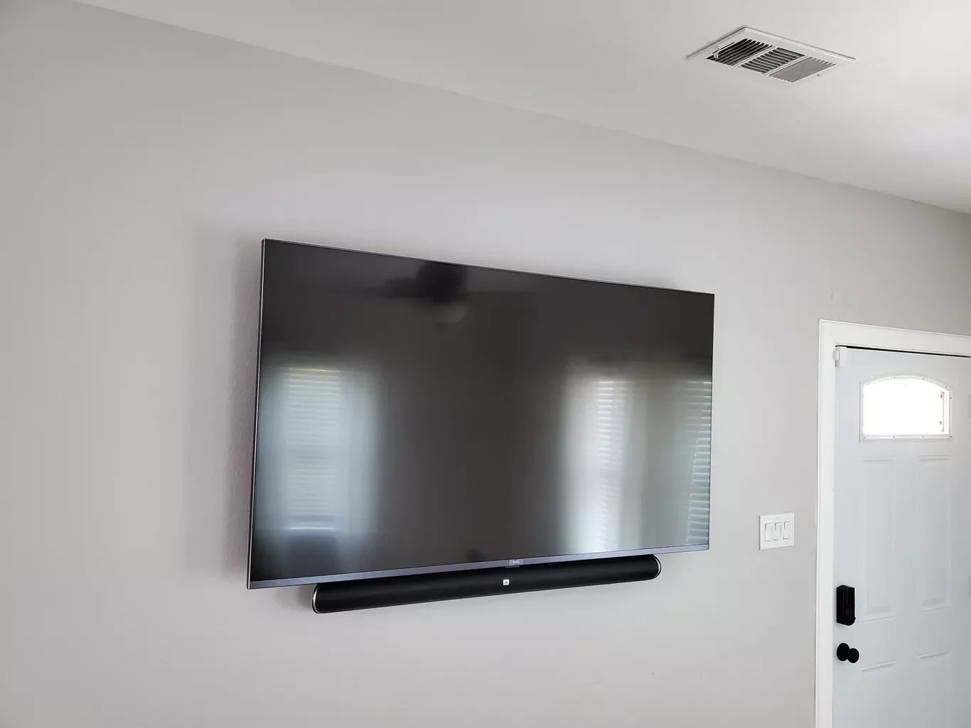 Flat-screen TV mounted on a white wall, with a soundbar below, near a white door with a small window above its handle.