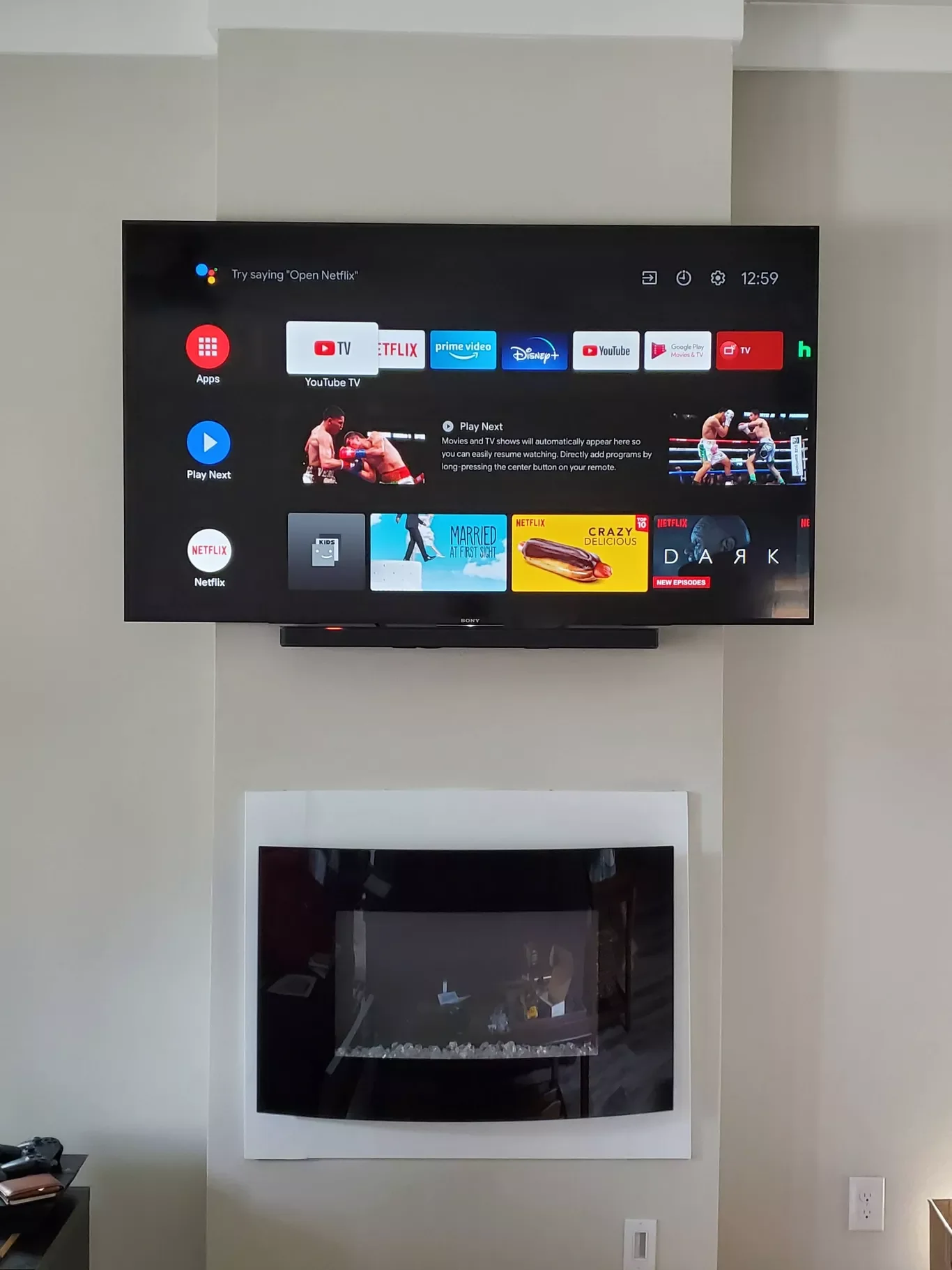 Wall-mounted TV displaying streaming app icons and options with a fireplace below it.