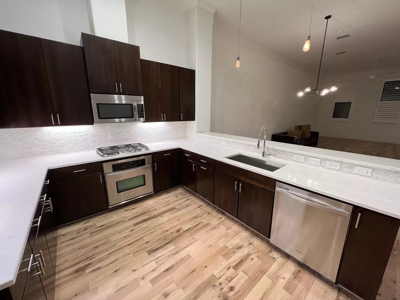 Modern kitchen with dark wood cabinets, stainless steel appliances, white countertops, and hardwood floors.