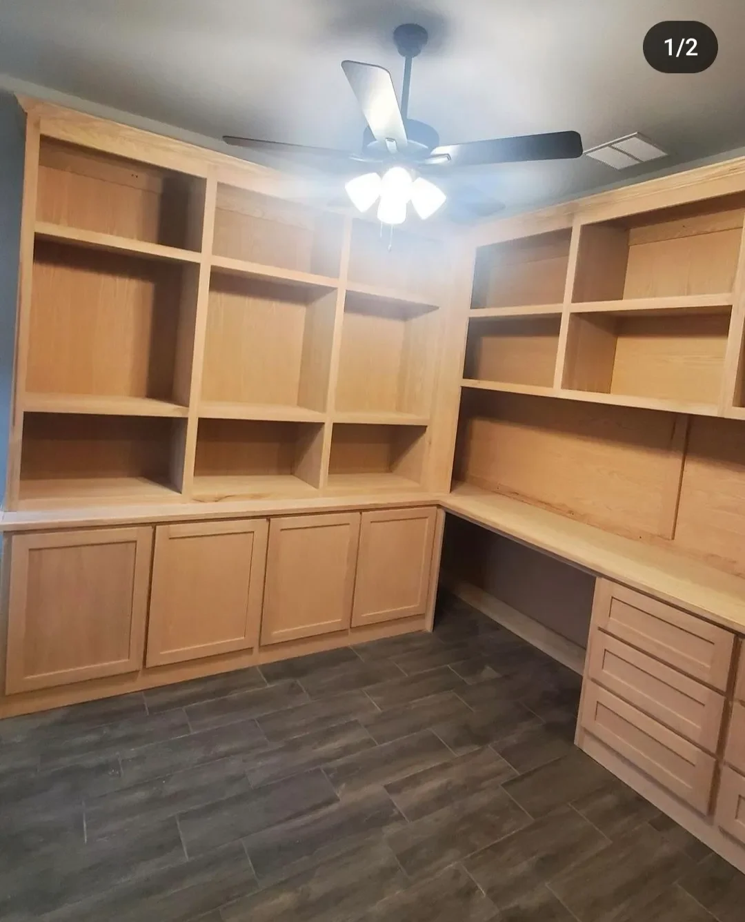 Empty wooden built-in shelves, cabinets, and drawers in a room with dark wood flooring, a ceiling fan, and measuring or utility openings.