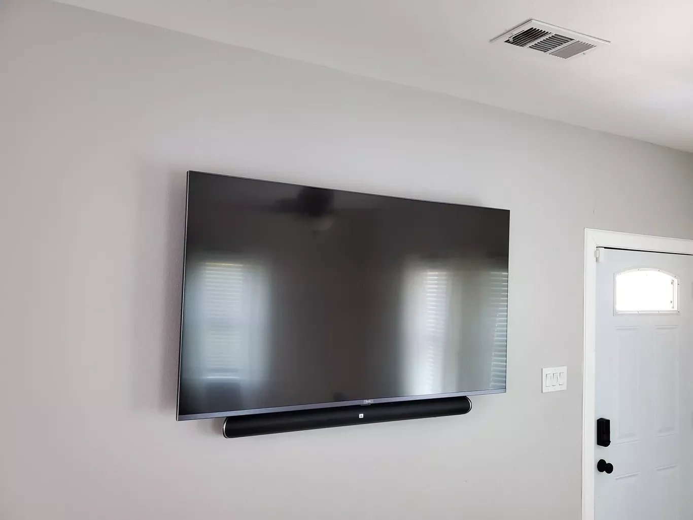 Flat-screen TV mounted on a white wall, with a soundbar below, near a white door with a small window above its handle.