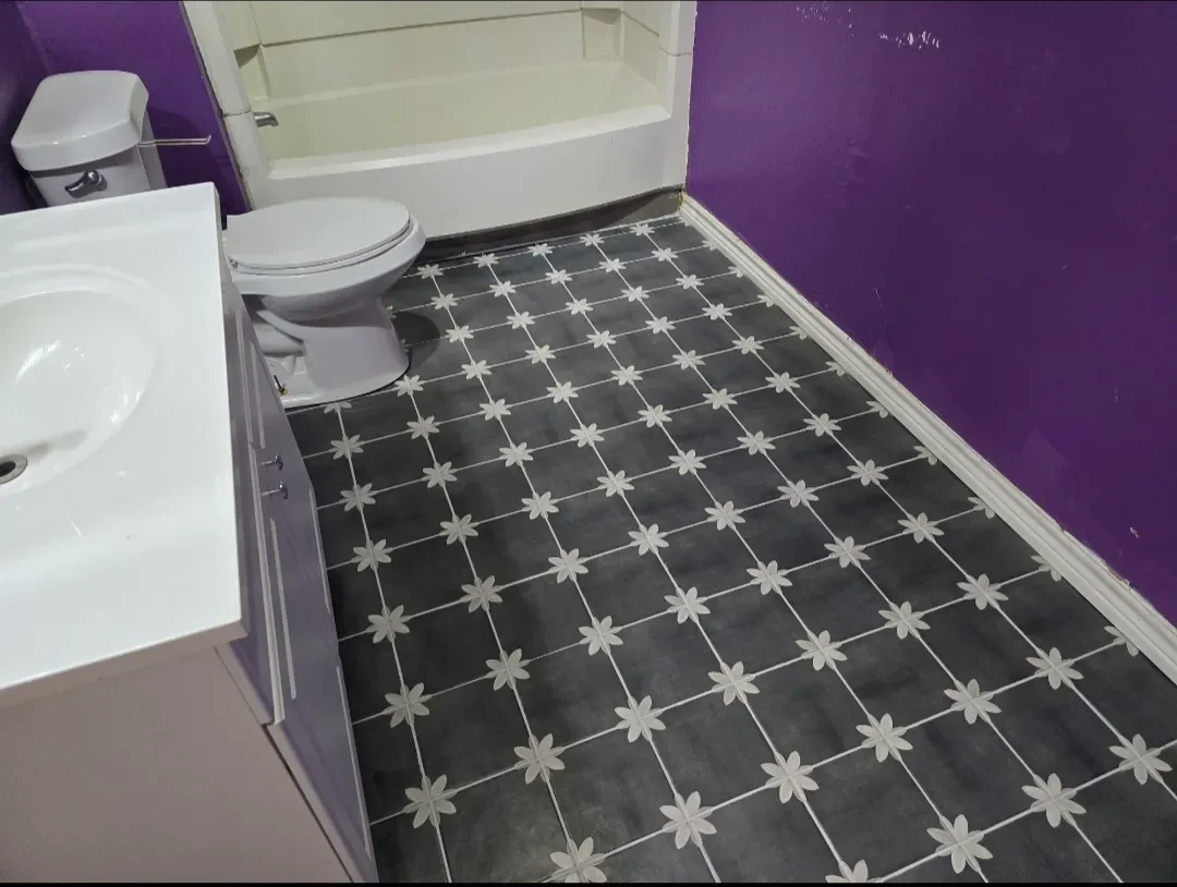 A bathroom with purple walls, a white sink, a toilet, a white shower with a curved rod, and gray tiles with white floral pattern on the floor.
