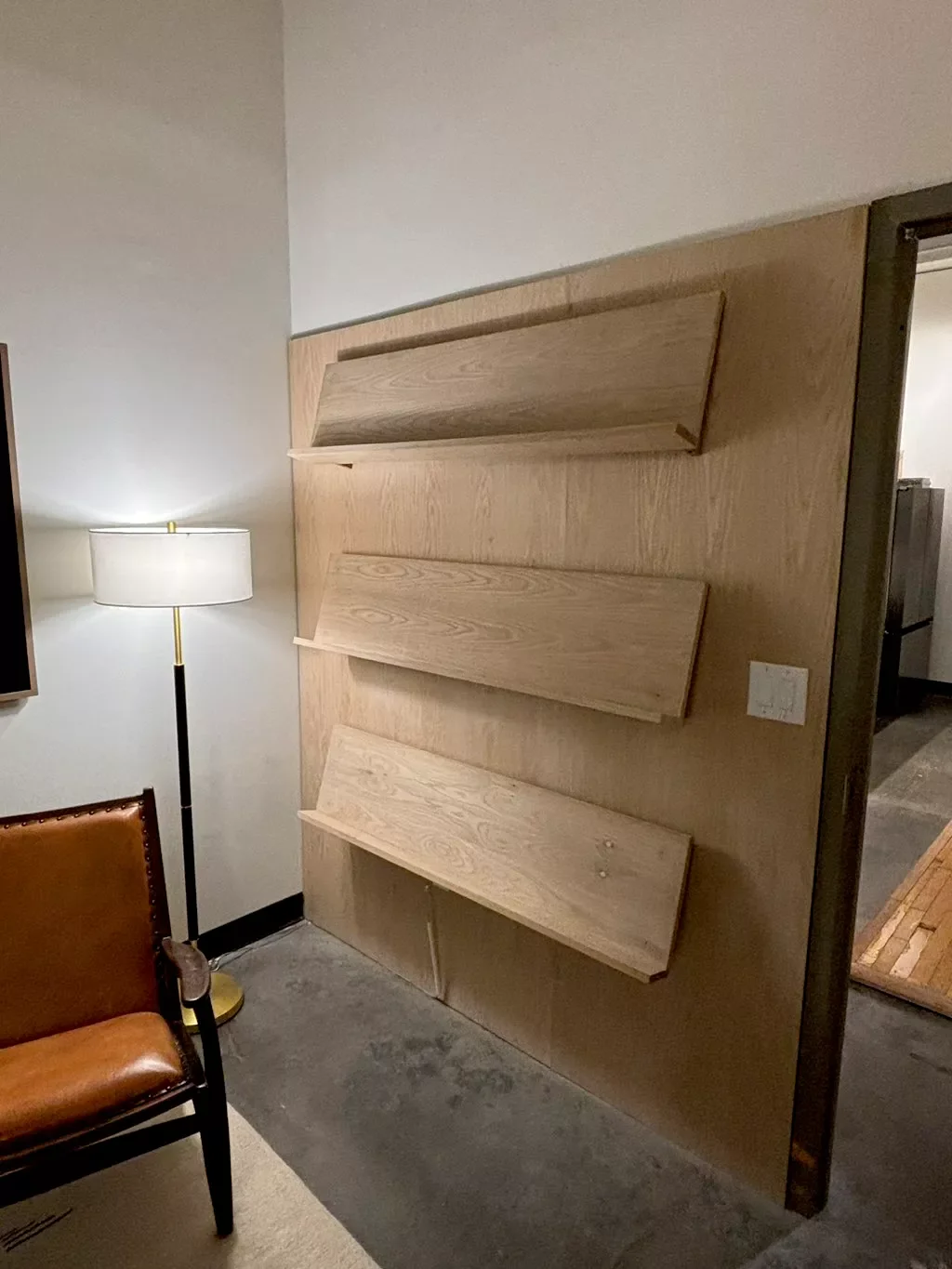 Wooden headboard with shelves in a room, next to a leather chair and a floor lamp.
