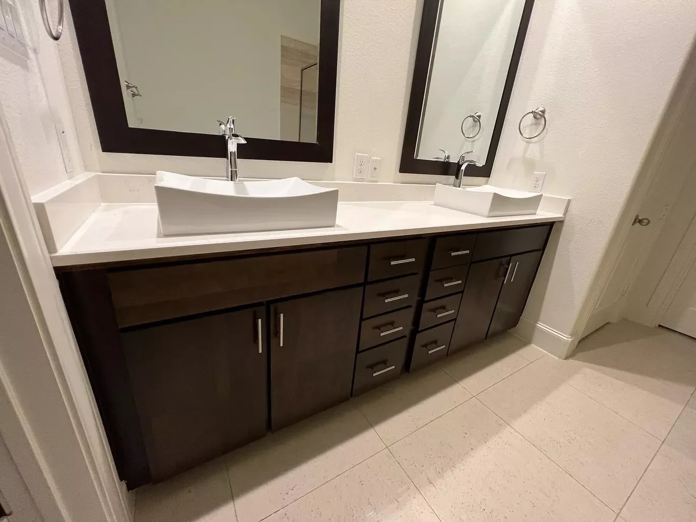 Double bathroom vanity with two rectangular vessel sinks, two mirrors, and dark wood cabinets with silver handles.