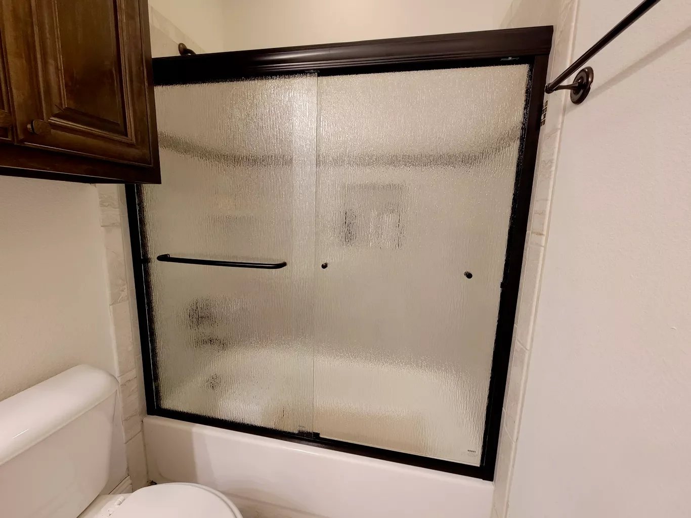 Bathroom with toilet, brown cabinet, and frosted glass sliding shower door.
