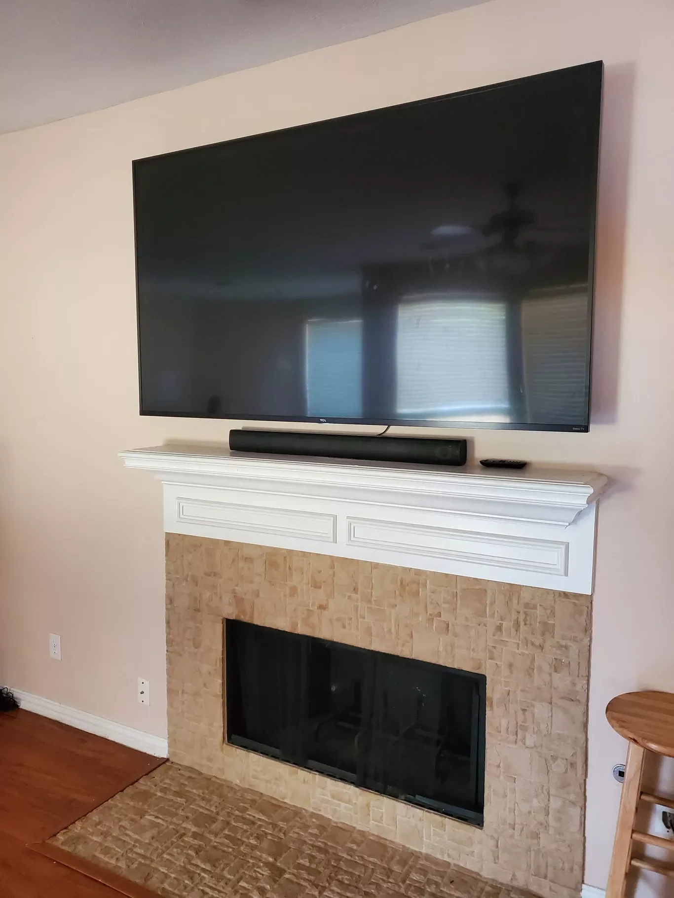 A flat-screen TV mounted above a fireplace with a white mantel, in a room with beige walls and hardwood floors.