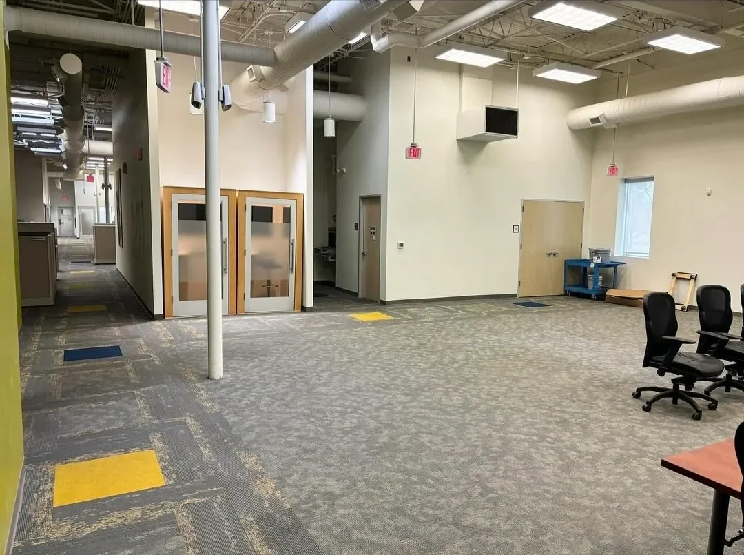 Empty office space with chairs, a window, a blue cart, and some closed doors.