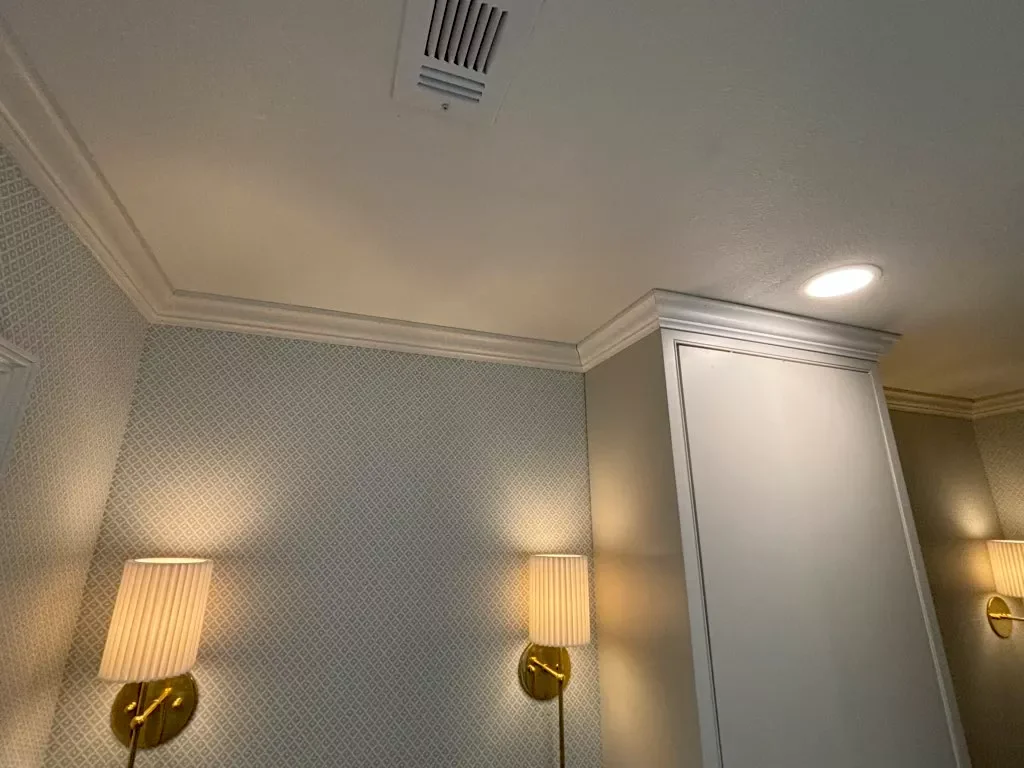 Interior view of a room with patterned wallpaper, wall-mounted lamps, a ceiling vent, and a column with white paneling.