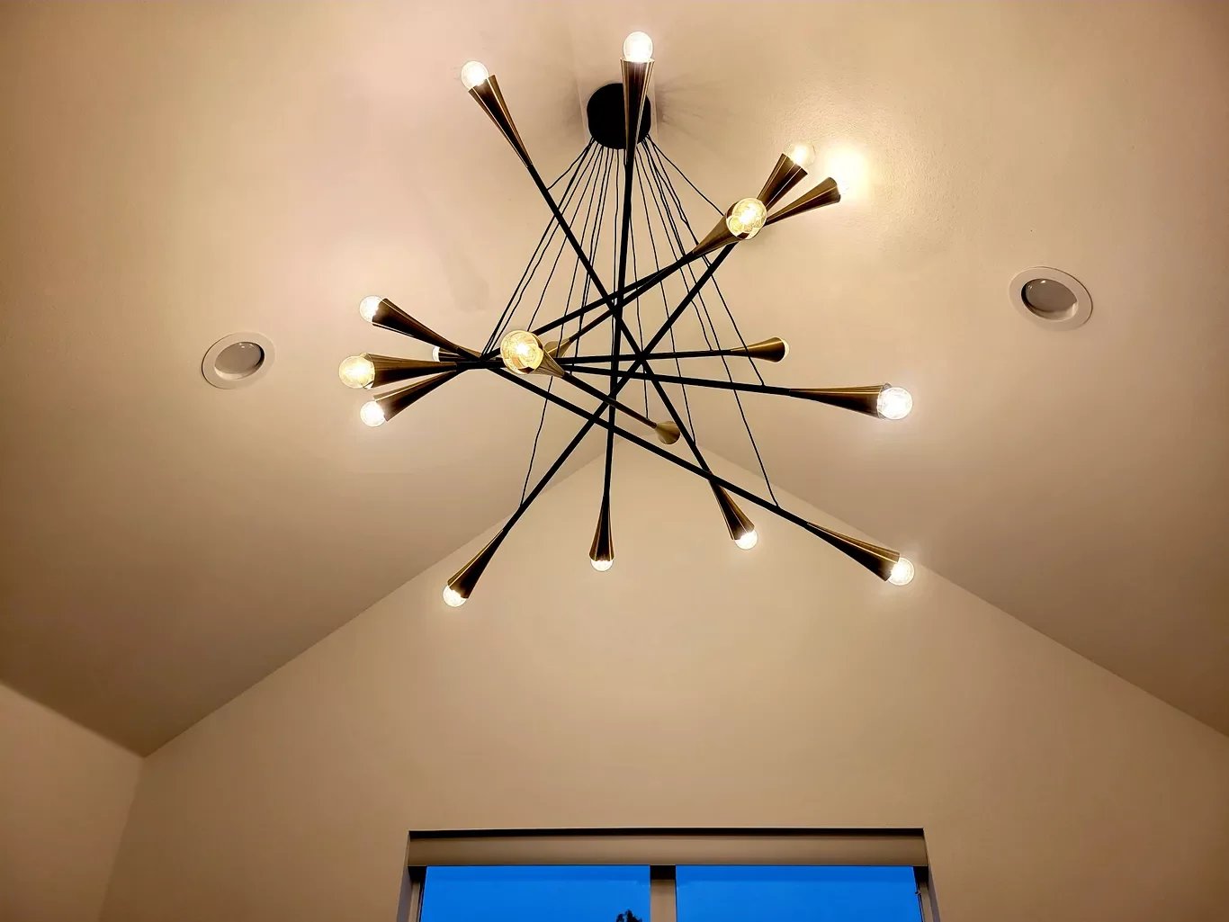 Modern chandelier with multiple arms and exposed bulbs hanging from a white ceiling