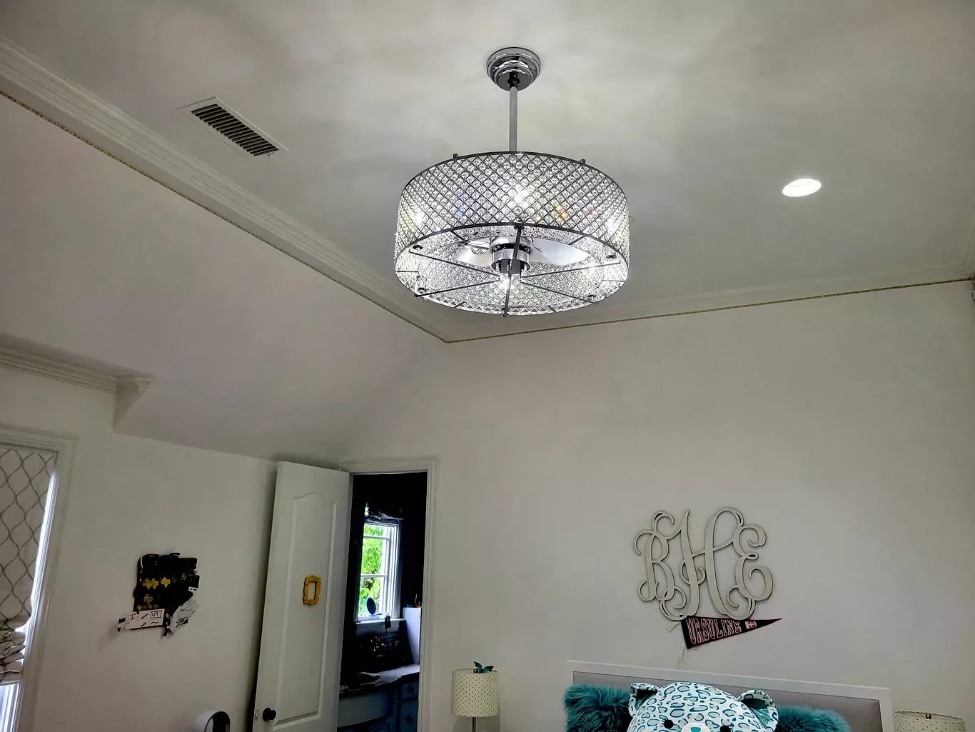 Ceiling light fixture with a mesh design in a room with white walls and ceiling, with a window and door in the background, and some decor on the wall.