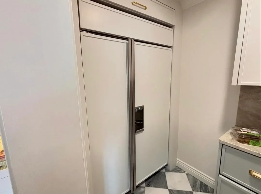 A white side-by-side refrigerator with an ice and water dispenser in a kitchen corner, next to a white cabinet and marble countertop.