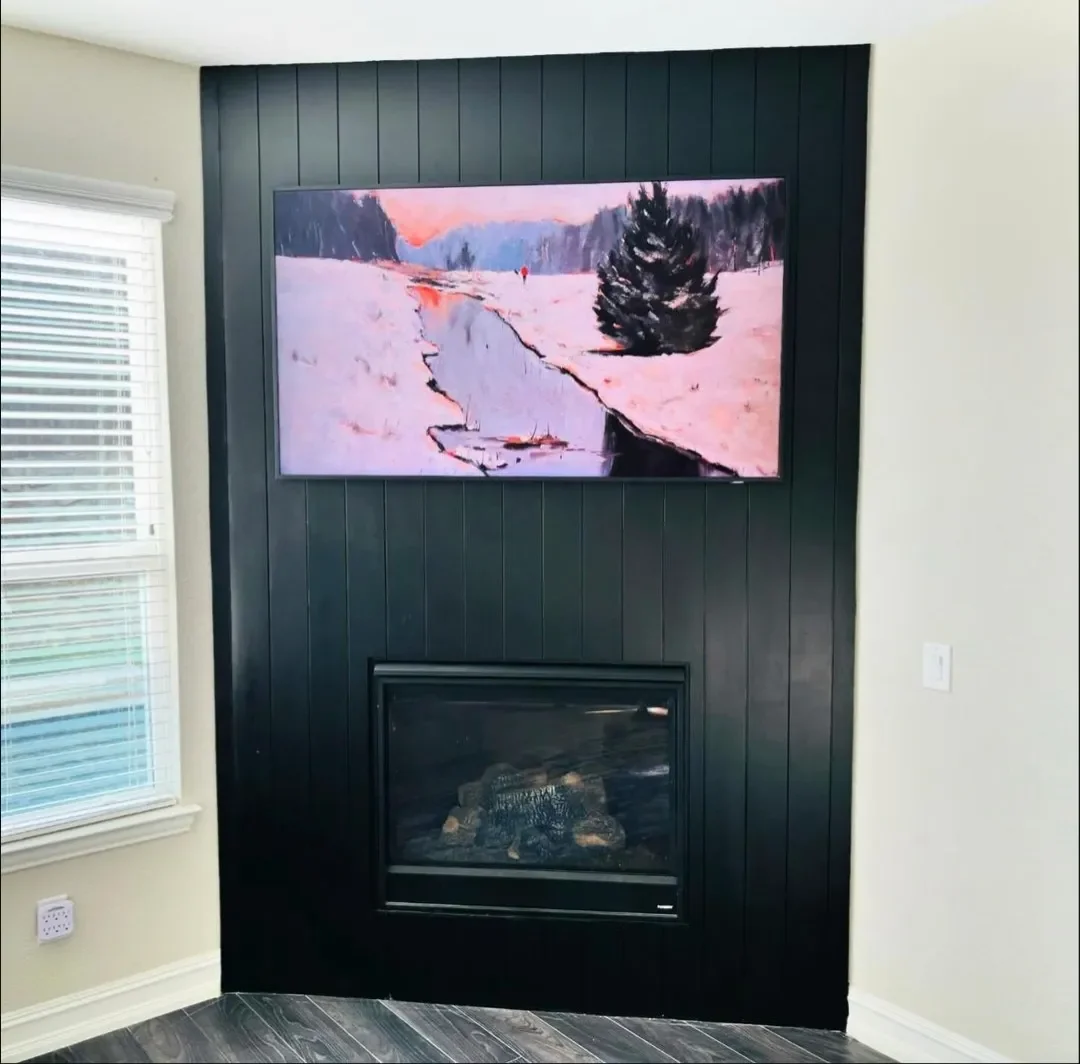 Living room corner with a black-paneled wall, a fireplace, and a mounted flat-screen TV displaying a winter landscape with snow, trees, and a sky at sunset.