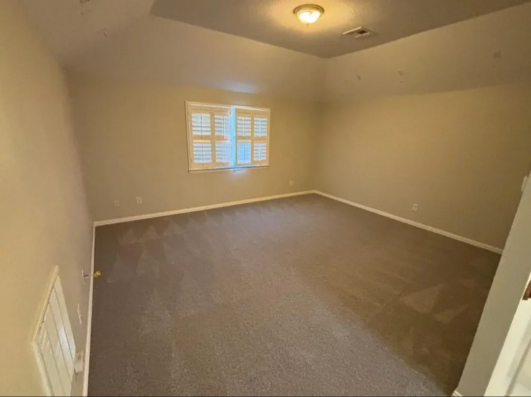 Empty room with beige walls, a single window with shutters, carpeted floor, and ceiling light.