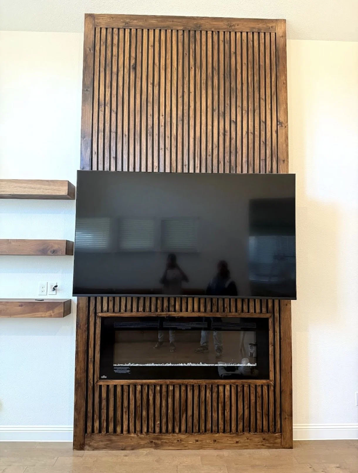 Wall-mounted wooden entertainment unit with a flat-screen TV and a built-in electric fireplace.
