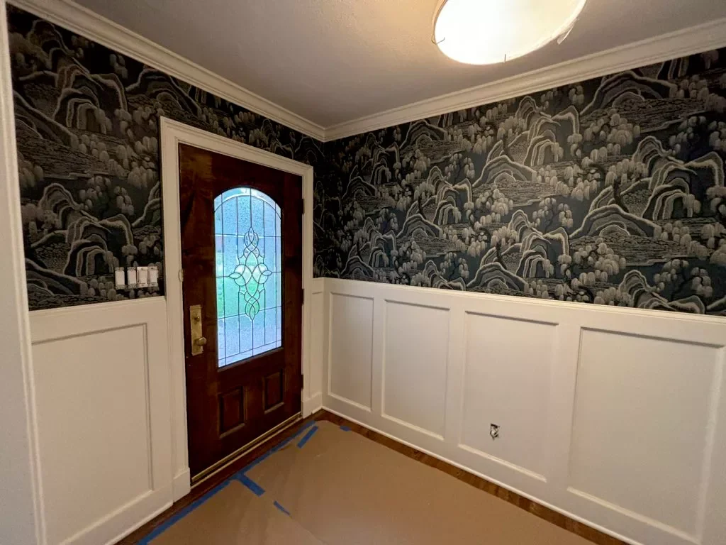 Entryway with decorative wallpaper, a wooden front door with a stained glass window, and white wainscoting on the walls.