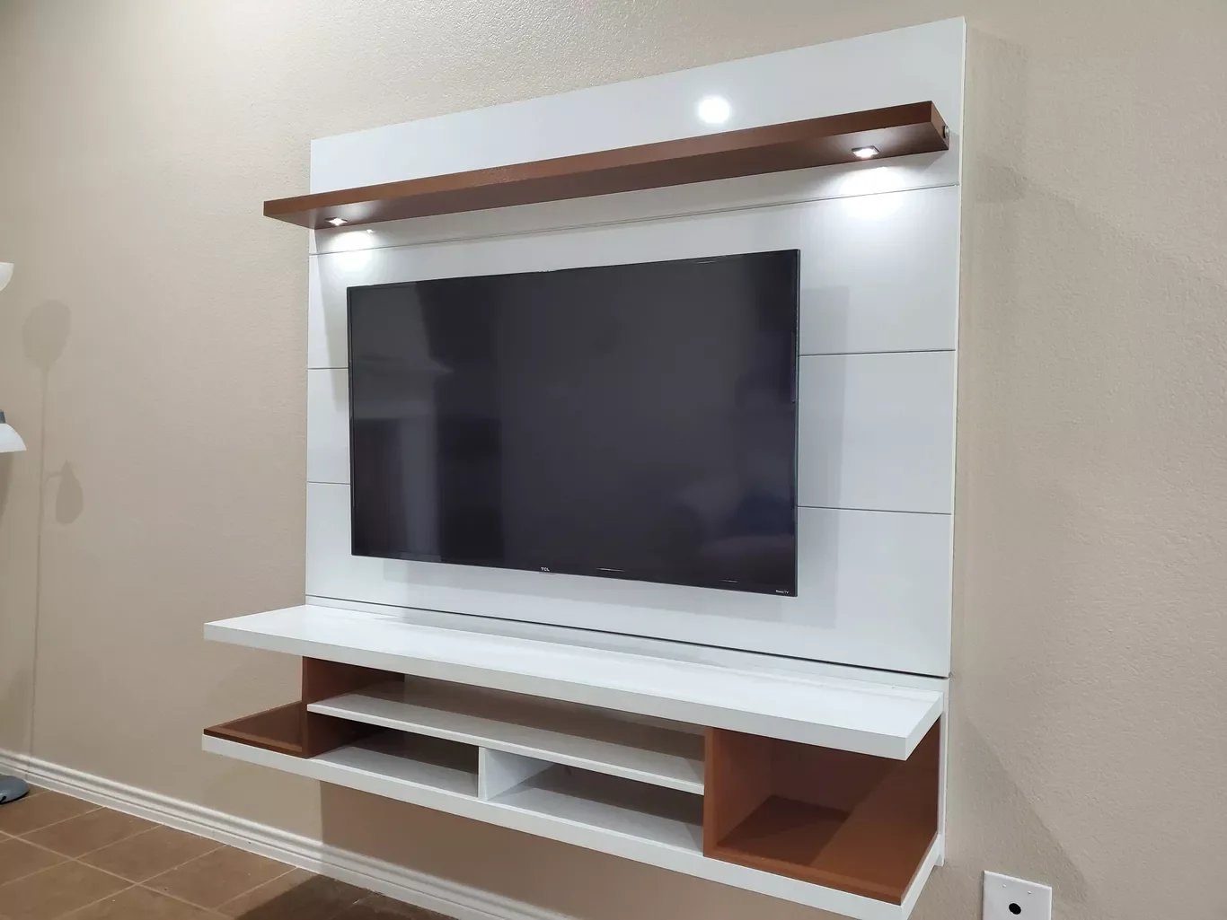 Modern wall-mounted entertainment center with a flat-screen TV and wooden shelves with built-in lighting.