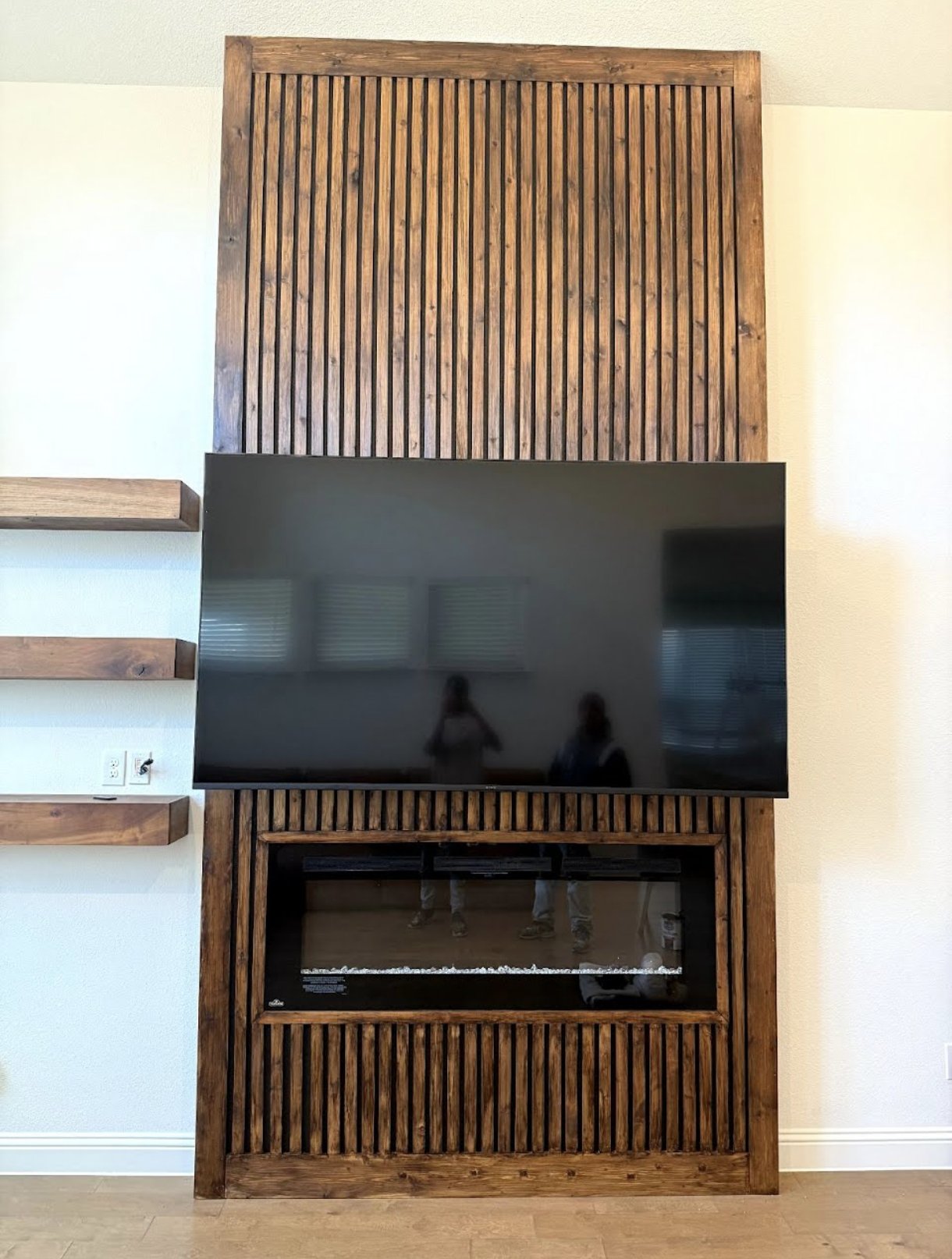 Wall-mounted wooden entertainment unit with a flat-screen TV and a built-in electric fireplace.