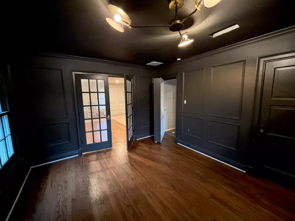 Empty room with dark gray walls and hardwood floor, French doors leading to another room, and a ceiling light fixture.