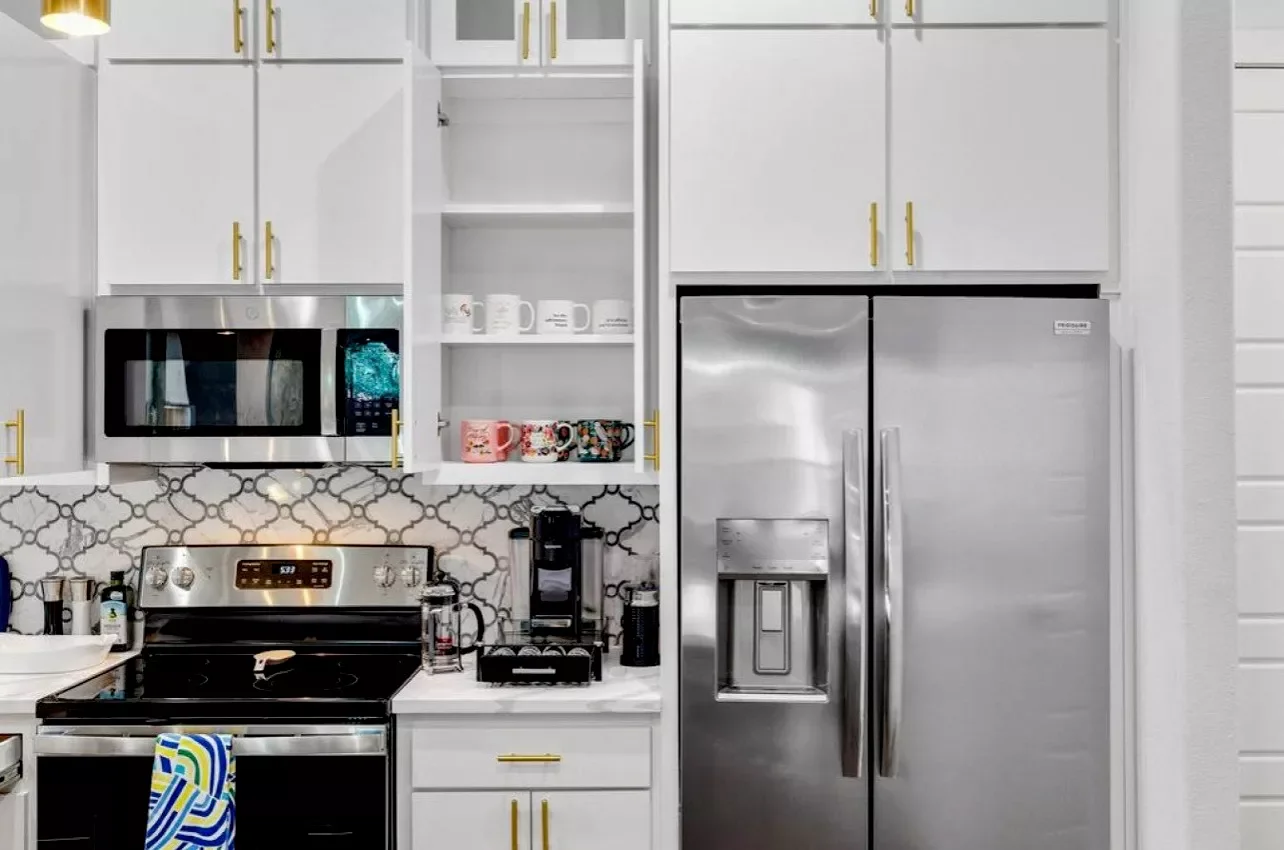 Kitchen with white cabinets, a stainless steel microwave, a double-door refrigerator, open shelves with mugs, a stove, and a coffee maker.