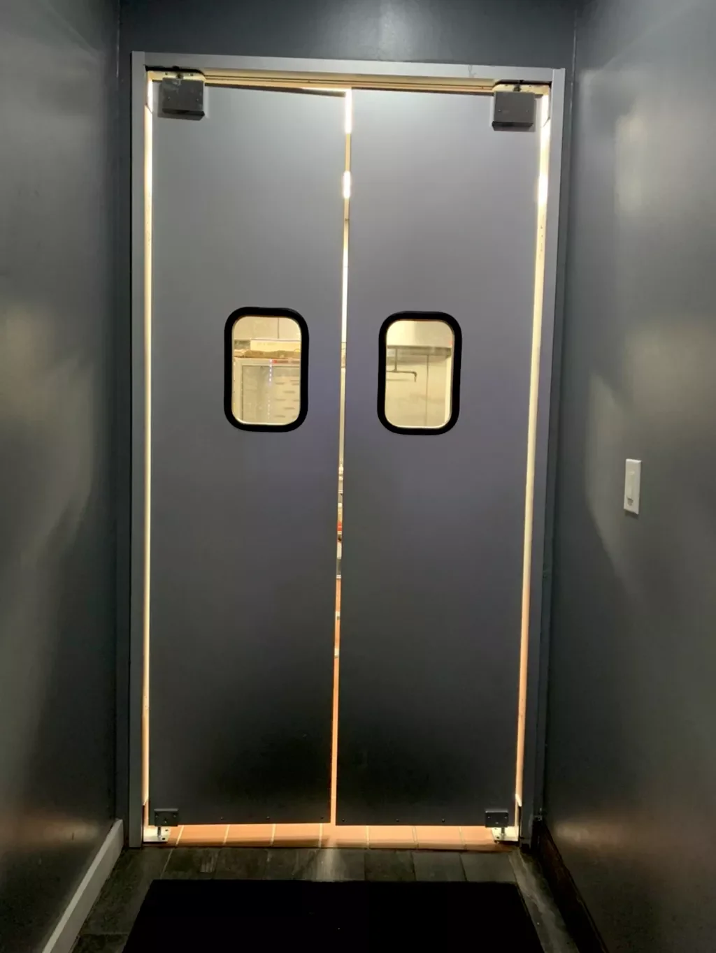 Gray double doors with small rectangular windows, leading to an industrial or commercial space.
