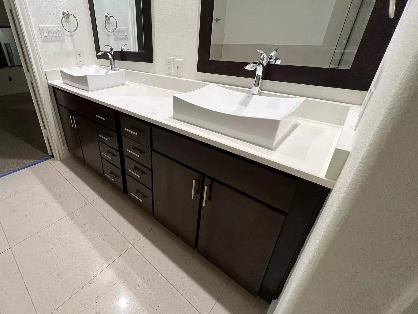 Double bathroom vanity with two vessel sinks, rectangular mirrors, dark wood cabinets, white countertop, and modern chrome faucets.
