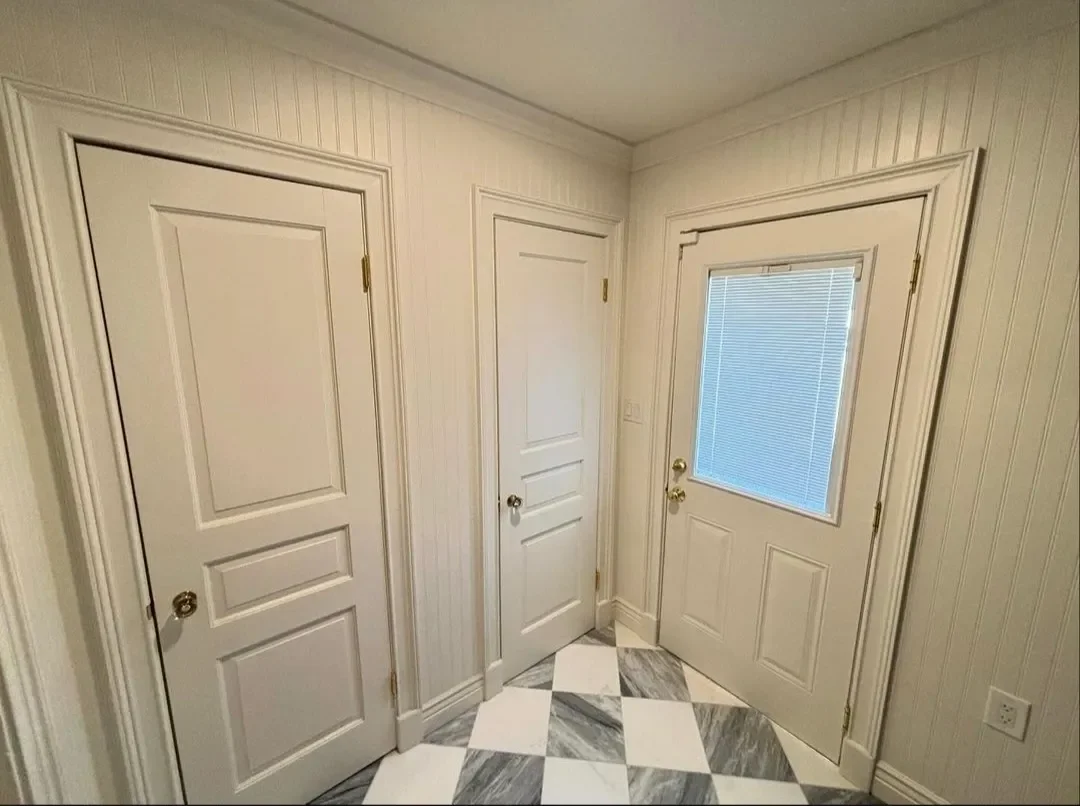A small entryway with three white doors, one with a window covered by blinds, and black-and-white checkered marble tile floor.
