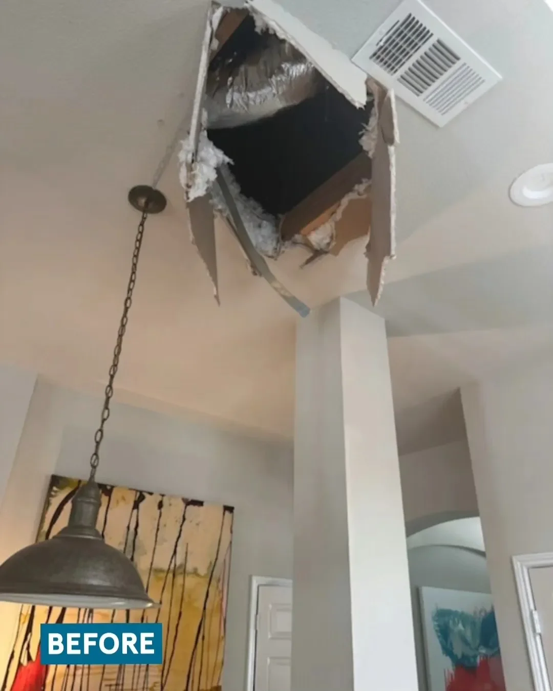 Ceiling with a large hole exposing ductwork and insulation, a hanging light fixture, and a painting on the wall.