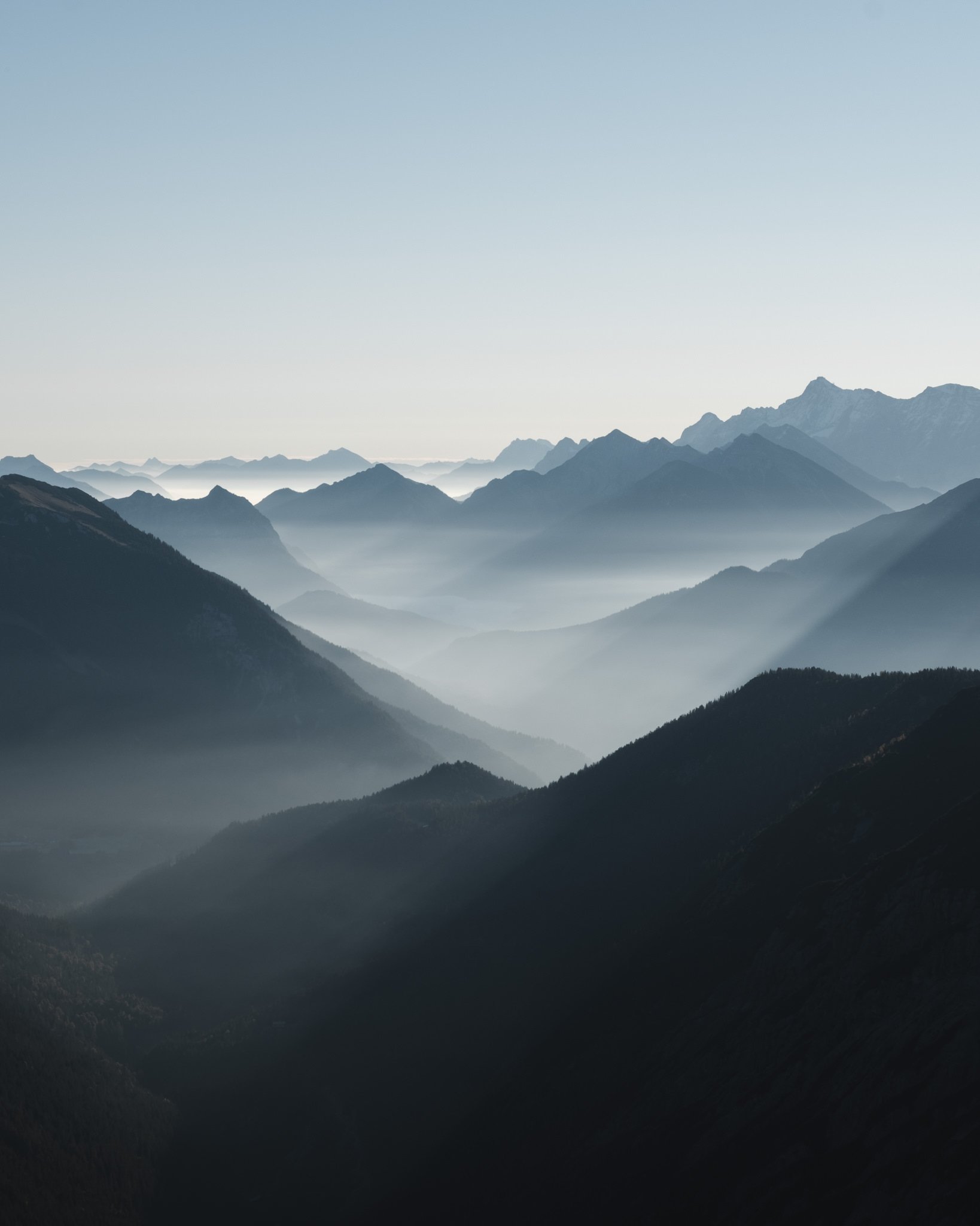 Bergketten im Nebel bei Sonnenaufgang, neblige Atmosphäre, ruhiges Bergpanorama, beruhigende Naturansicht.