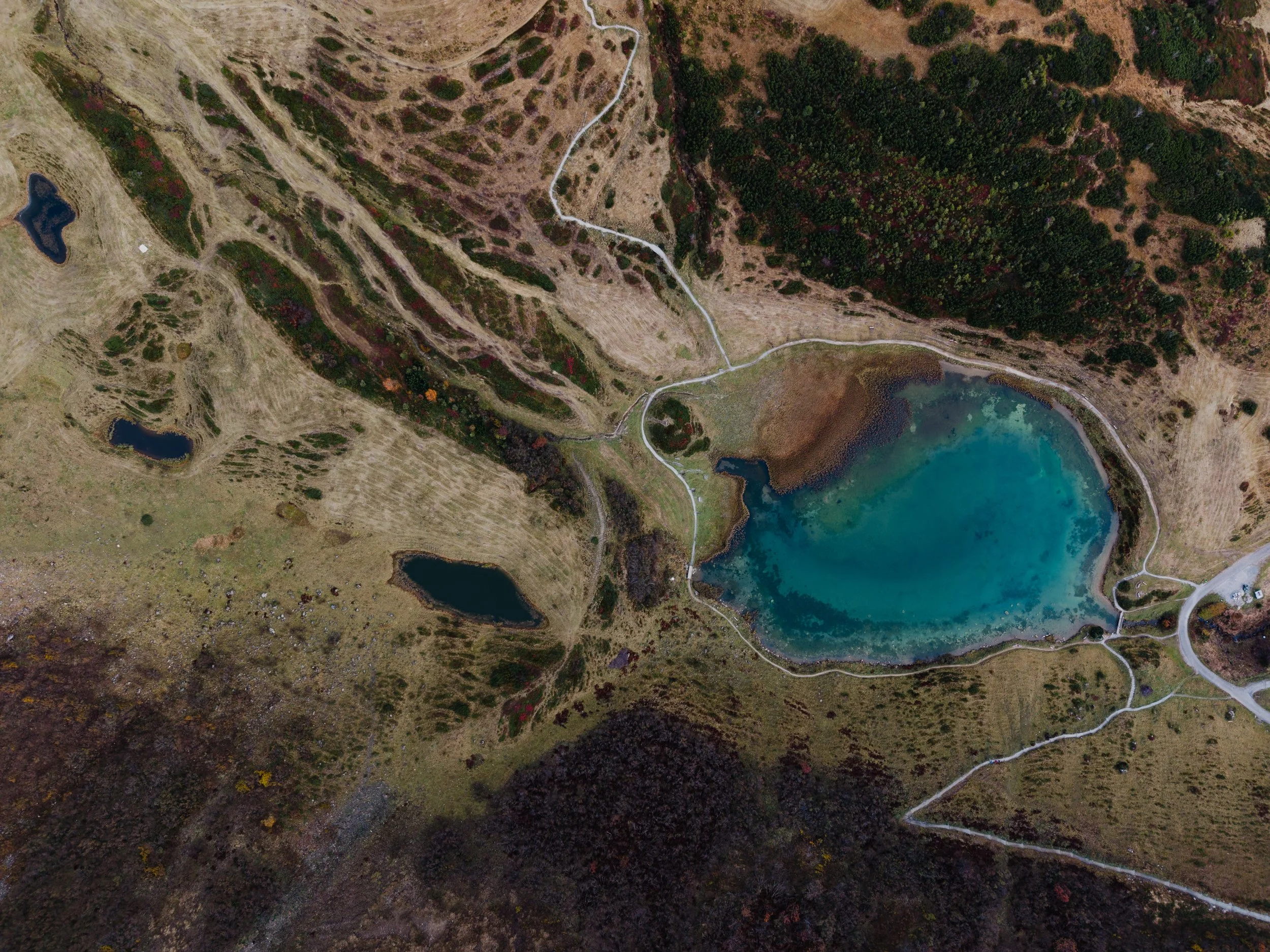 Luftaufnahme eines Sees inmitten von Bergen mit Wanderwegen und Waldgebiet.