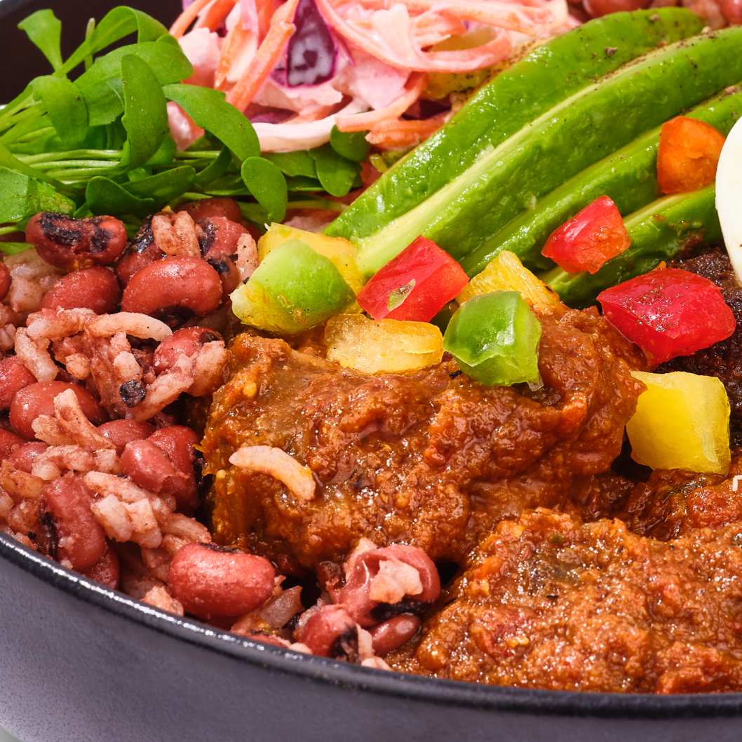 Close-up of a vibrant West African bowl featuring savory beans, tender ground meat simmered in a rich tomato-based sauce, fresh green beans, sliced avocado, diced red and green bell peppers, and crisp coleslaw and salad greens.