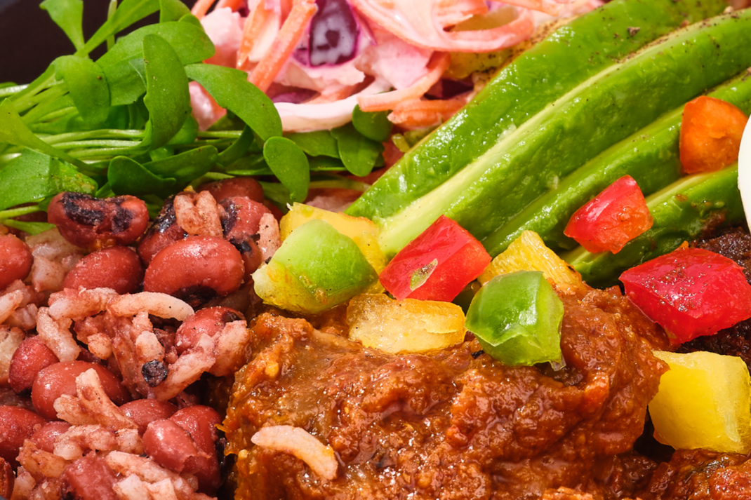 Close-up of a rich, colorful West African dish featuring savory beans, vibrant greens, finely chopped fresh vegetables, and tender meat simmered in a deep, aromatic sauce.
