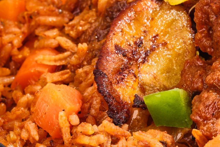 Close-up of a vibrant West African plate featuring golden-fried plantains, aromatic mixed rice with vegetables, and tender pieces of chicken, garnished with fresh green bell peppers.