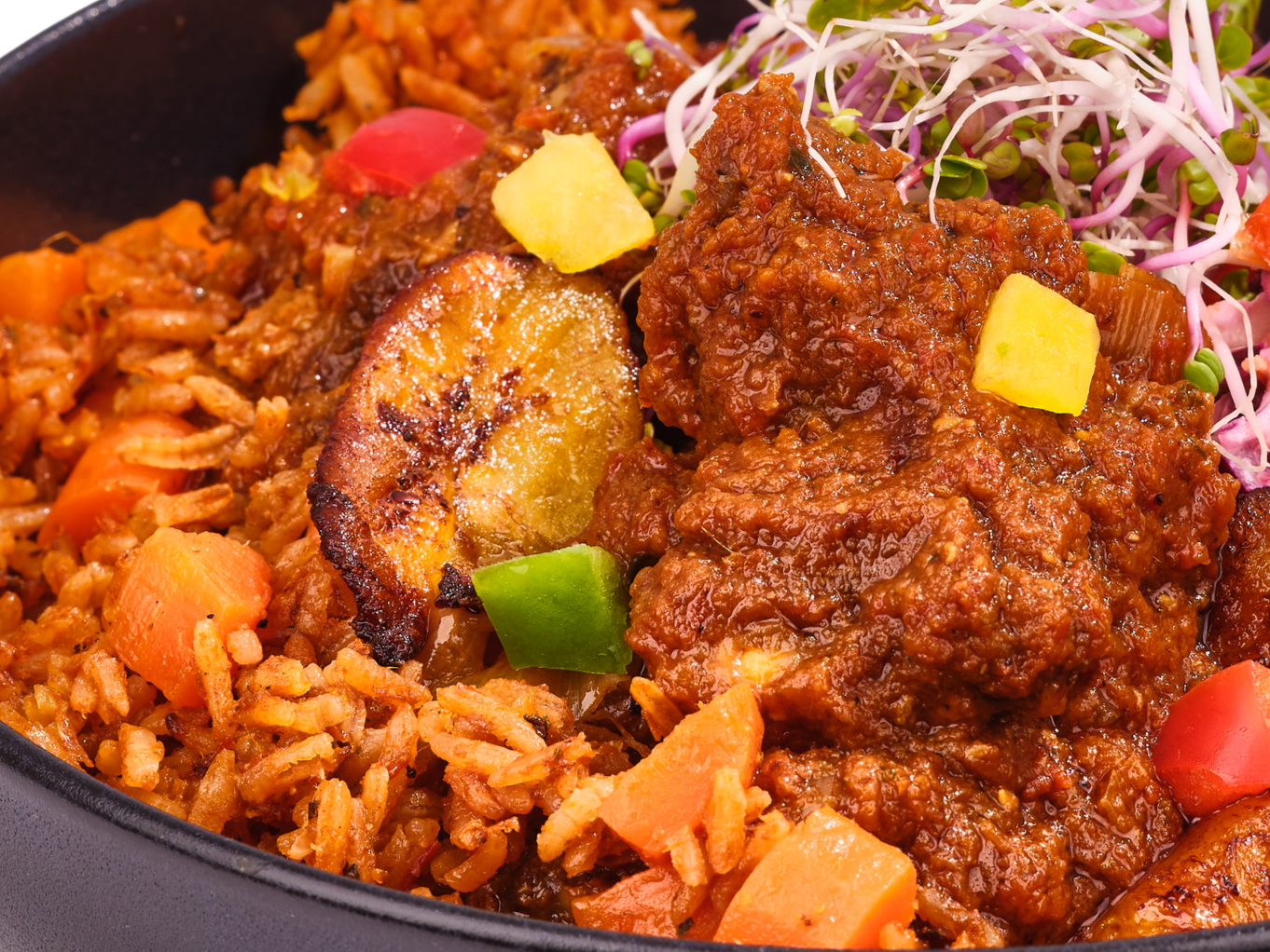 Close-up of a vibrant West African plate featuring fragrant rice, golden-fried plantains, tender chicken in a rich, spiced red sauce, and a fresh side salad with crisp sprouts and finely chopped vegetables.