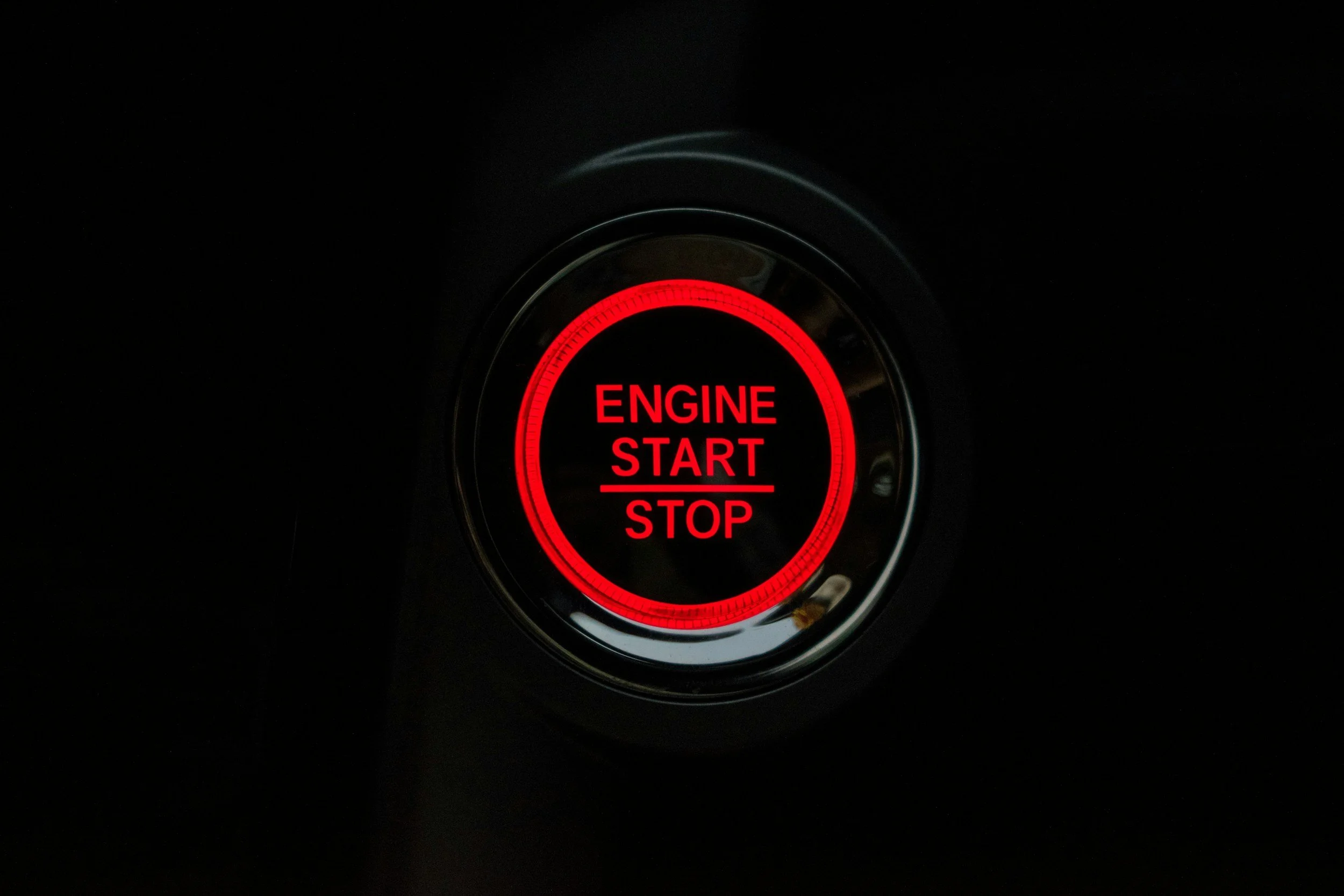 A close-up view of a car's start/stop engine button illuminated in red against a dark background.
