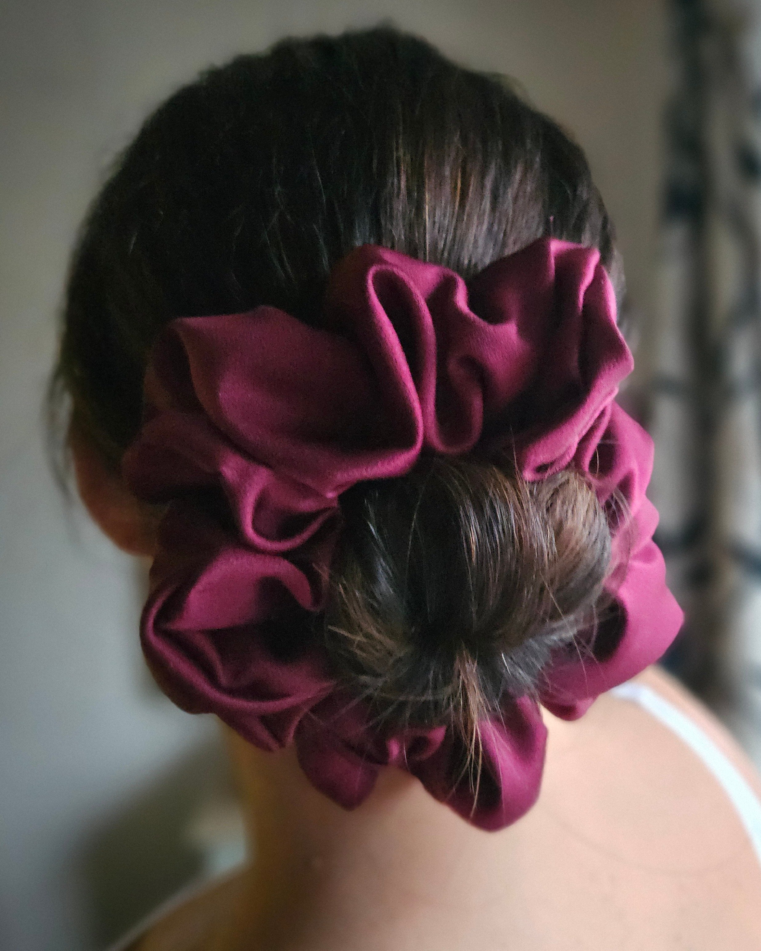 Close-up of a person's head with dark hair, partially covered by a pink scrunchie. The person is wearing a pink shirt.
