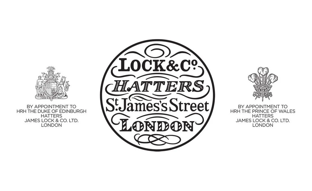 Vintage-style logo with text reading "Lock & Co. Hatters, St. James's Street, London" inside a circle, flanked by two crests indicating royal appointments, one with the Duke of Edinburgh and the other with the Prince of Wales.