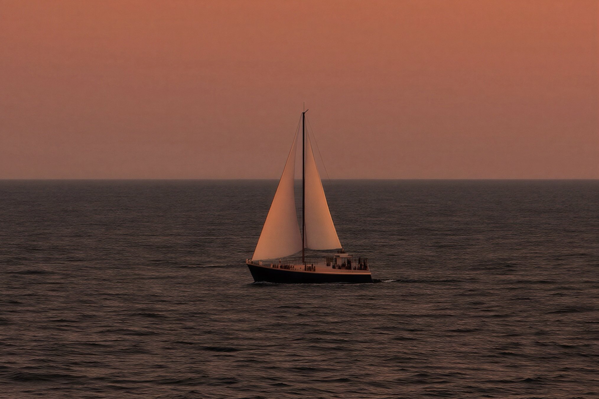 Un velero navegando en el mar durante un atardecer con cielos rosados y nubes dispersas.