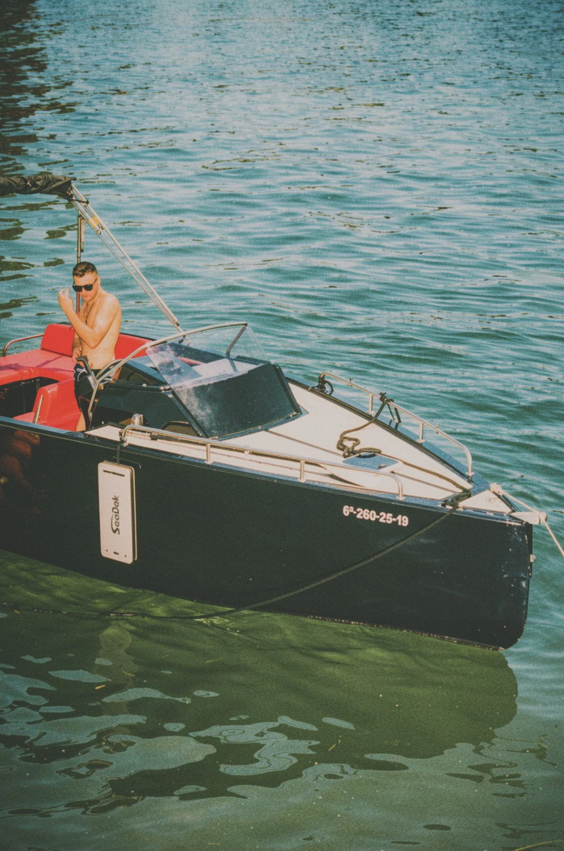 Joven con gafas de sol en una lancha en el agua. Con el lateral del barco escrito "SeaDek".