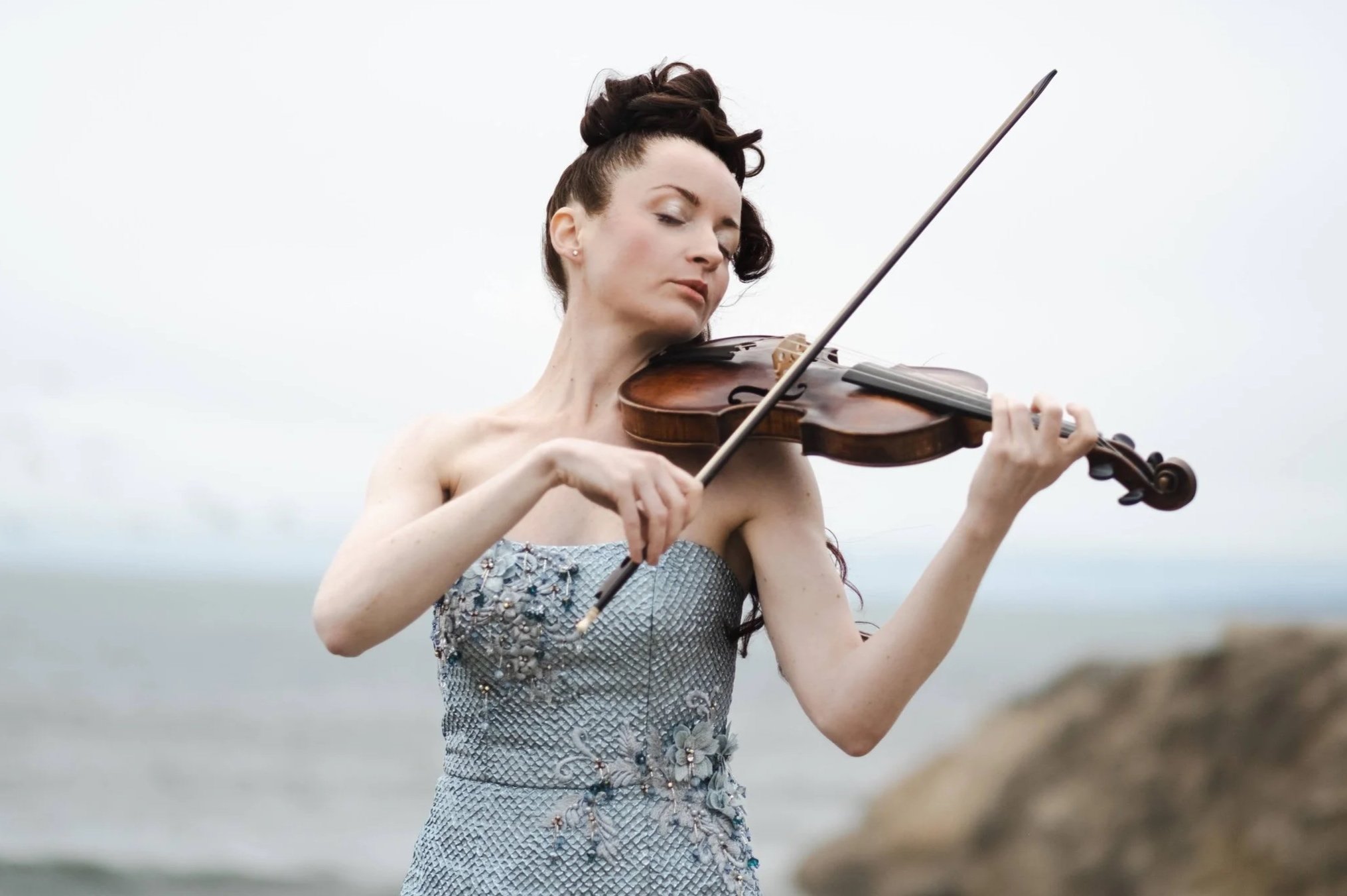 Concert violinist  Tatiana performing outdoors against a dramatic sky.