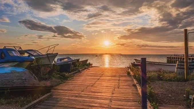 Sunset over a calm body of water viewed from a wooden dock with boats on the left and a small pier on the right.