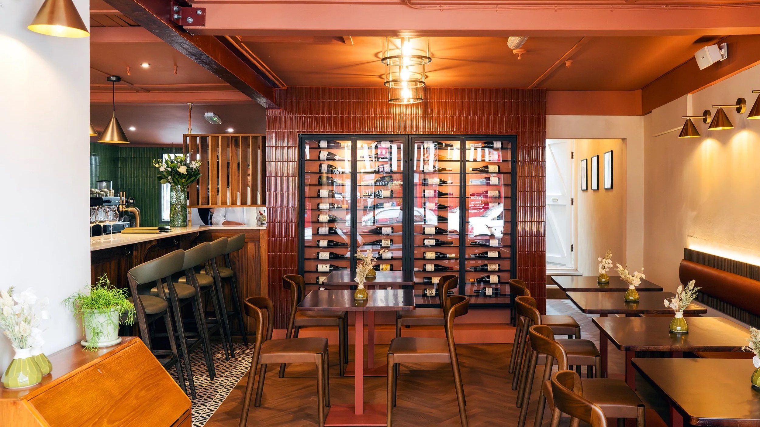 Interior of a restaurant or cafe with a wine display cabinet, wooden tables and chairs, floral centerpieces, and stylish lighting fixtures.