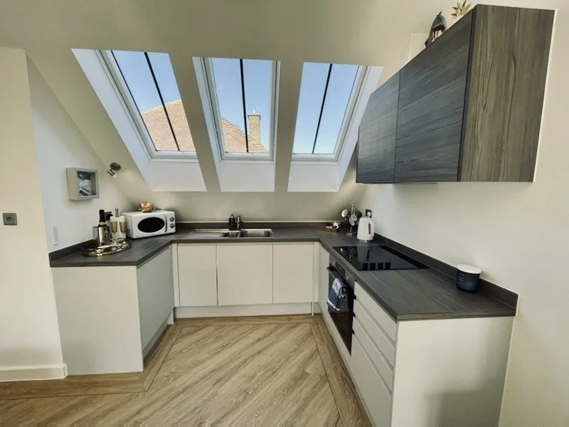 Compact kitchen with white cabinets, dark countertop, and large skylight windows.