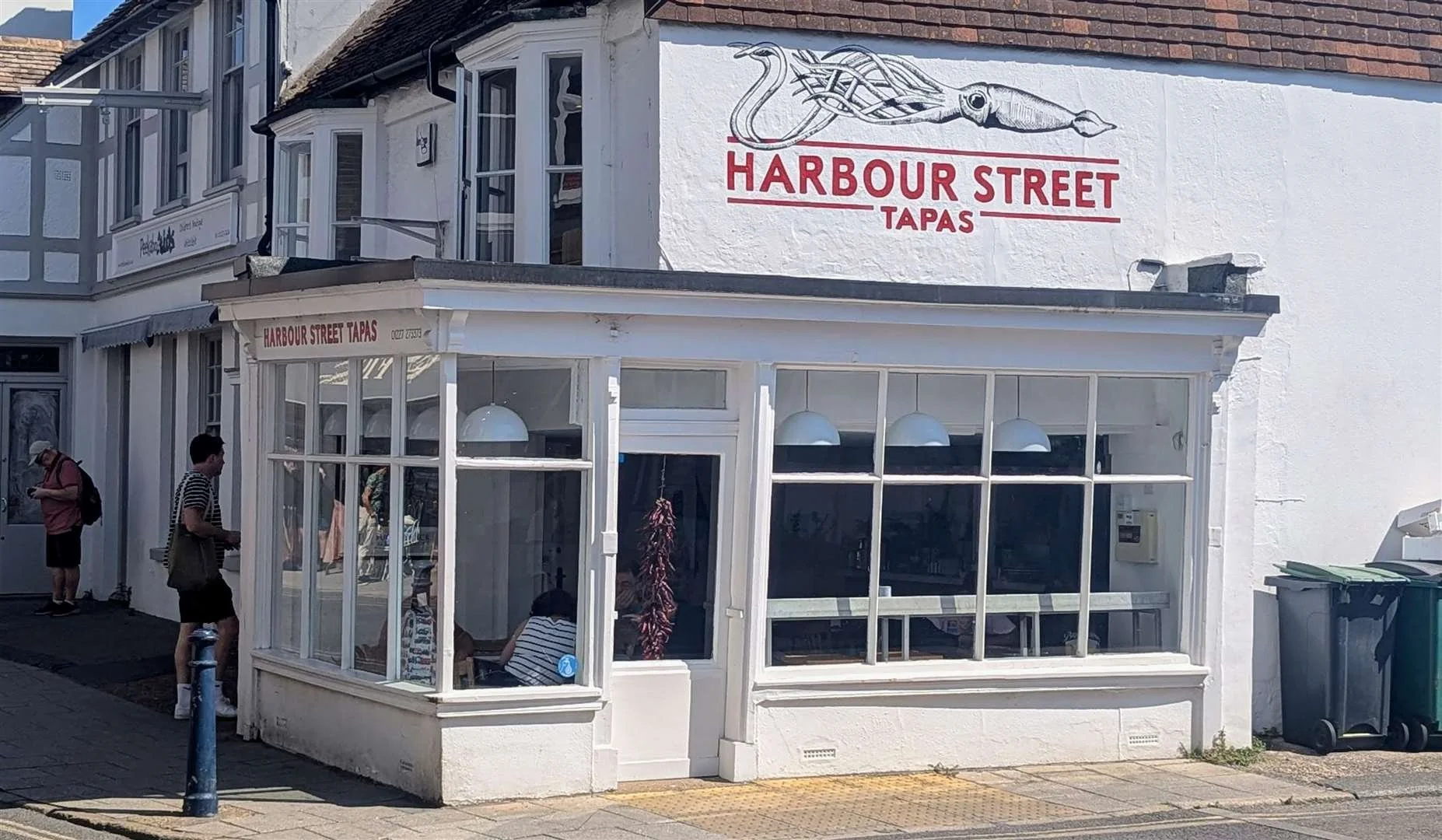 Exterior of a small restaurant named Harbour Street Tapas with a white building and large windows. Signage features a sketch of an octopus and the restaurant's name in red letters.