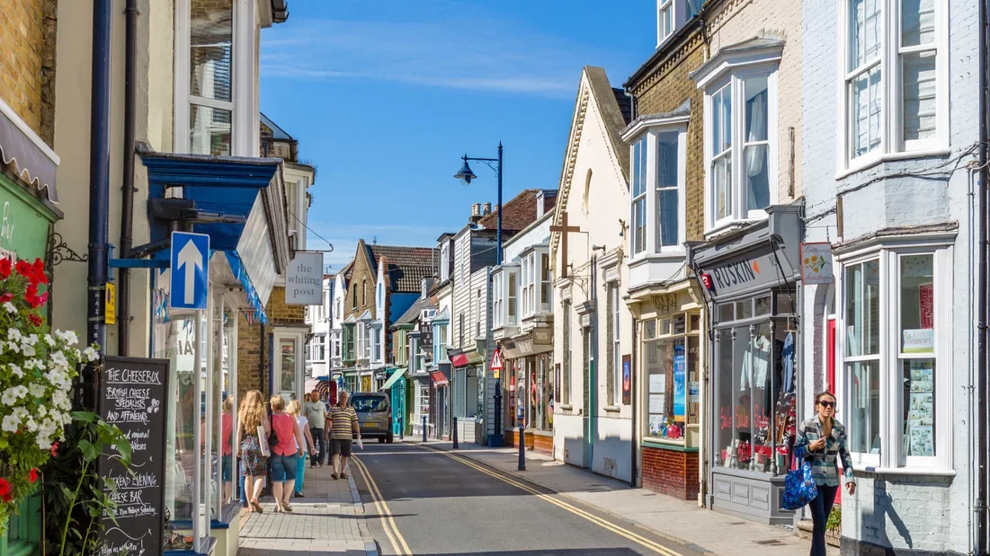View of a busy pedestrian street with shops and storefronts on both sides, people walking, and a clear blue sky above.