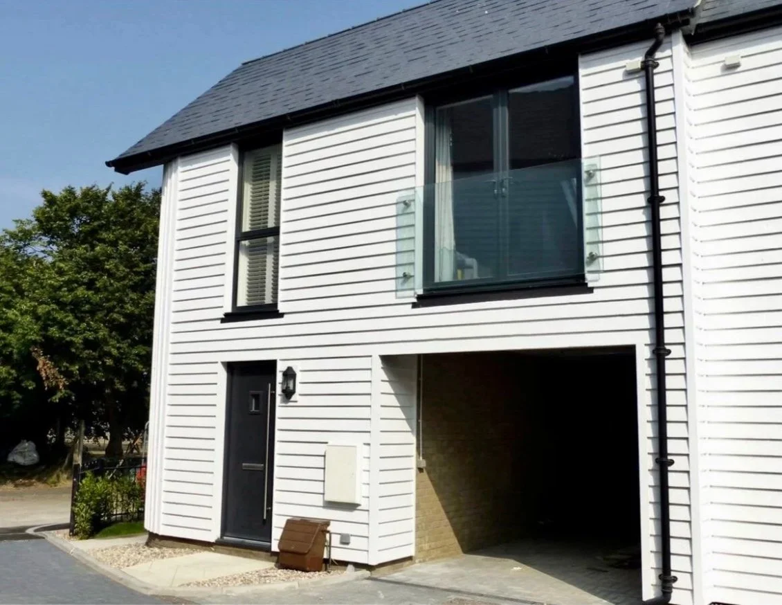 Front view of a modern two-story house with white siding, black window frames, and a small balcony with glass railing.