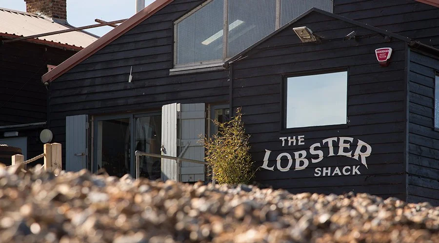 A black wooden building with a sign that reads "The Lobster Shack" and a small window.