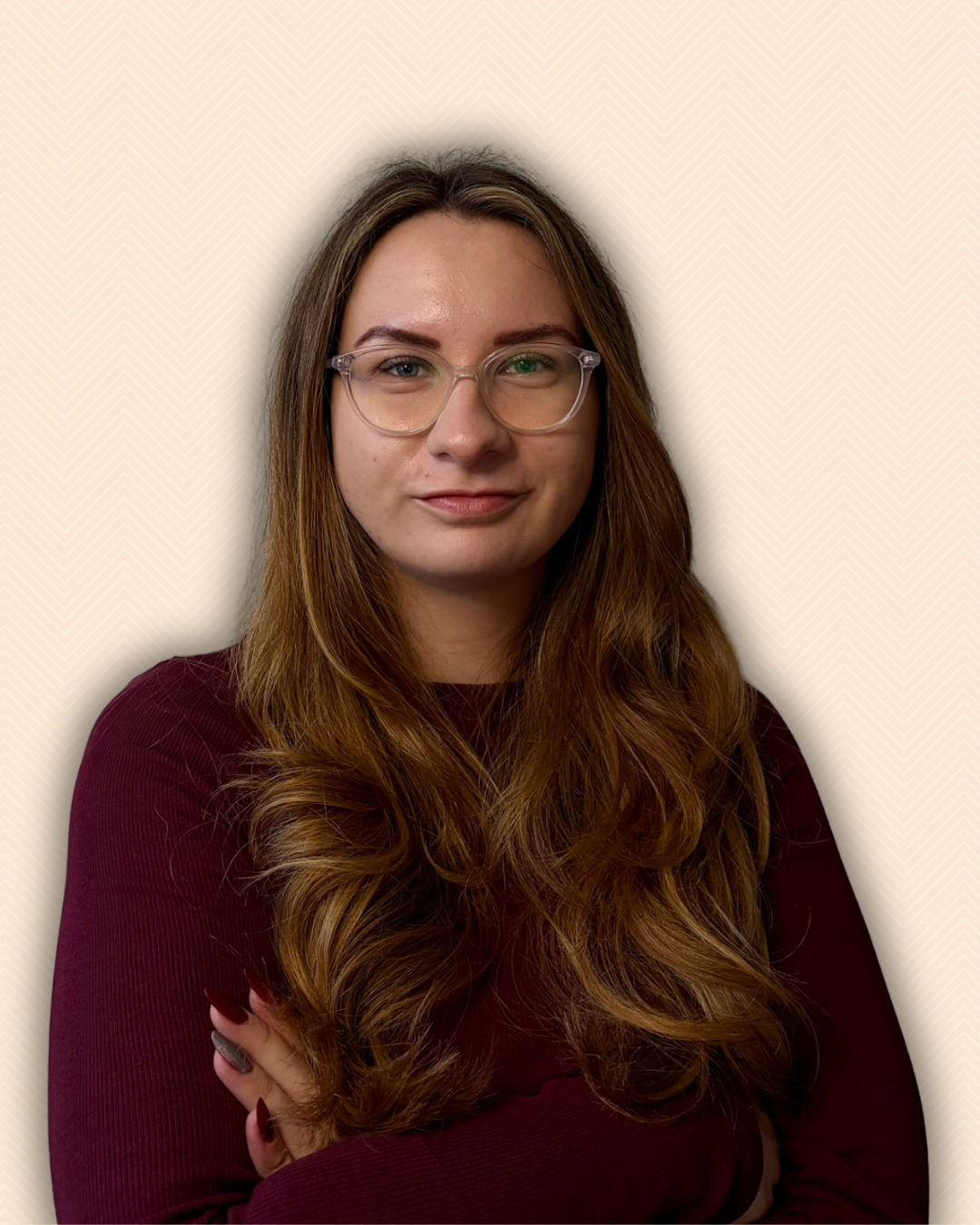 Porträt einer Frau mit Brille, lange braune Haare, dunklem Pullover, lächelnd, vor hellbeigem Hintergrund.