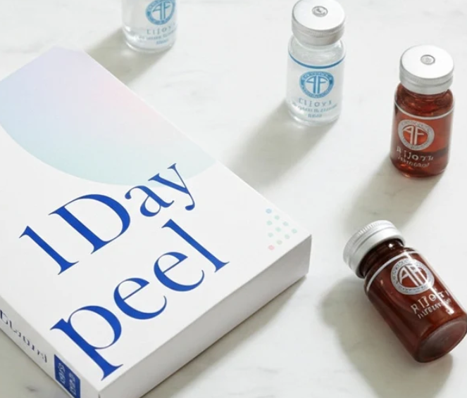 A box labeled '1 Day Peel' surrounded by small bottles of skincare products on a white surface.